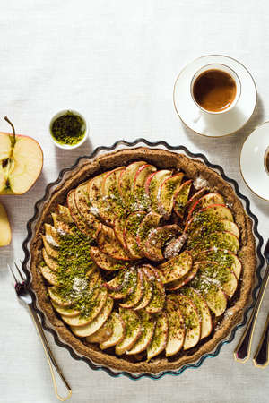 italian apple pie crostata with pistachio crumbs on the table with a white tablecloth and cups of coffee espressoの写真素材
