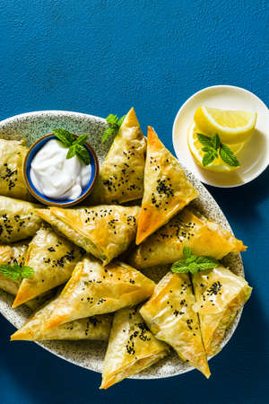 indian samosa made with phyllo with spicy potatoes and vegetables , served with yogurt, mint and lemon on a blue backgroundの写真素材