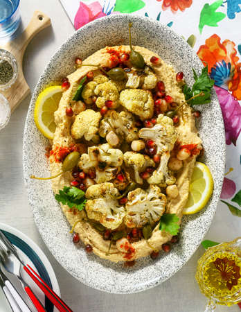 hummus with baked cauliflower and pomegranate seeds on a table with a bright colorful tableclothの写真素材