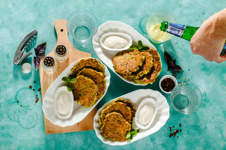 salted pancakes with zucchini and chickpea flour with spicy yoghurt sauce with beer on the table. summer vegan snack for family or lunch for friendsの写真素材