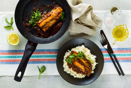 fillet of pink salmon in tomato-coconut sauce in a non-stick frying pan with parsley on a table with a linen tablecloth. healthy family food with basmati riceの写真素材
