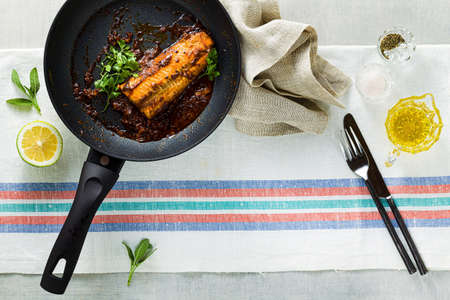 fillet of pink salmon in tomato-coconut sauce in a non-stick frying pan with parsley on a table with a linen tablecloth. healthy family foodの写真素材