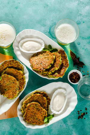 salted pancakes with zucchini and chickpea flour with spicy yoghurt sauce with beer on the table. summer vegan snack for family or lunch for friendsの写真素材