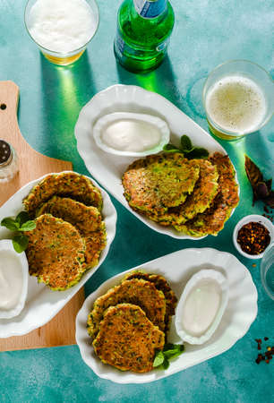 salted pancakes with zucchini and chickpea flour with spicy yoghurt sauce with beer on the table. summer vegan snack for family or lunch for friendsの写真素材