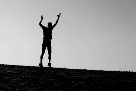 man silhouette with raising hands on low horizon with blurred background in black and white photo