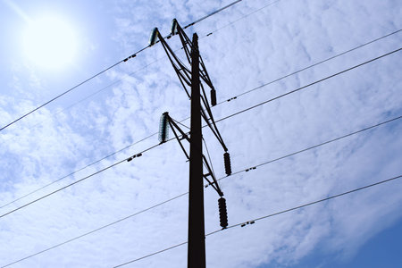 power line on background of shining sun on blue sky with clouds