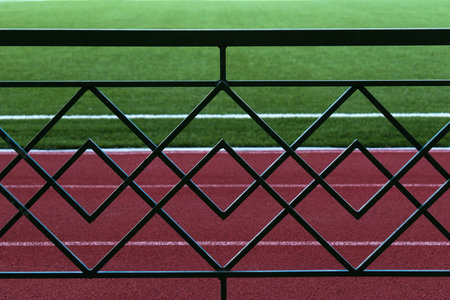 metal fence on blurred background of running track and green grass of stadium