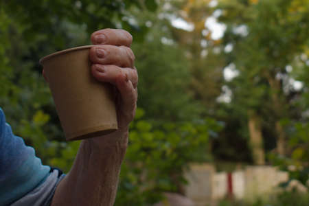 elderly woman hand holding cup of coffee on blurred background of green parkの写真素材