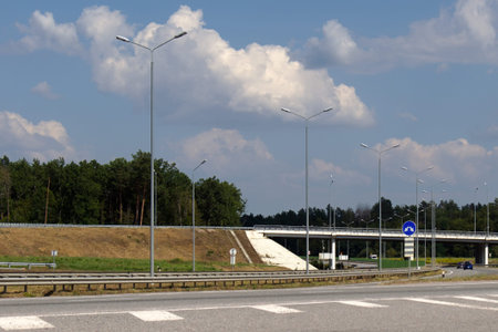 overpass over the freeway, lighting pillars along the road, blurred foreground, blue sky with white...