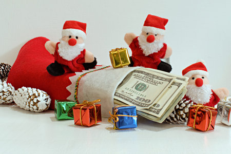 funny santa claus toys with christmas gift boxes and dollars on blurred white background