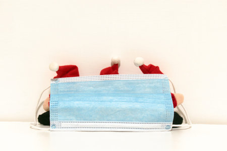 funny santa claus toys hiding behind antivirus protective medical masks on blurred white backgroundの写真素材