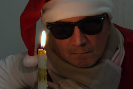 middle aged man in black glasses and christmas hat looks at burning candleの写真素材