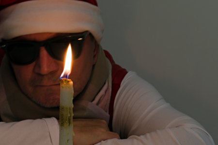 candle with bright burning fire close-up on blurred background of a man in black glasses and christmas capの写真素材