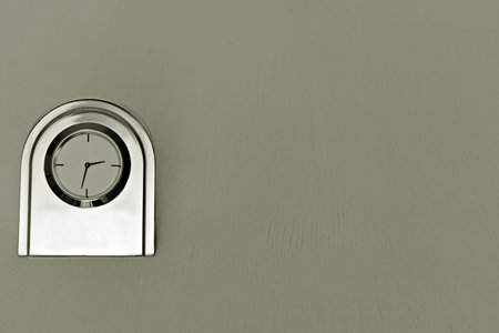 metal table clock with primitive face on blurred neutral gray background with space for text