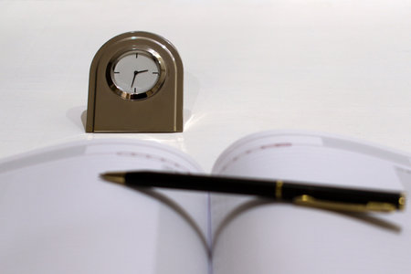 metal desk clock with blurred foreground with diary and ballpoint pen
