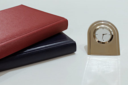 diaries organizers and metal table clock with reflection on white desk