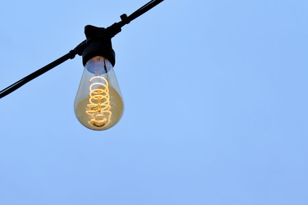 electric light bulb with bright glowing spiral inside close-up on blue background