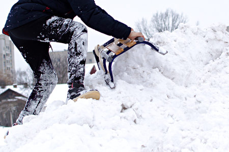 unrecognizable boy climbs a snowy mountain holding tightly to sledge