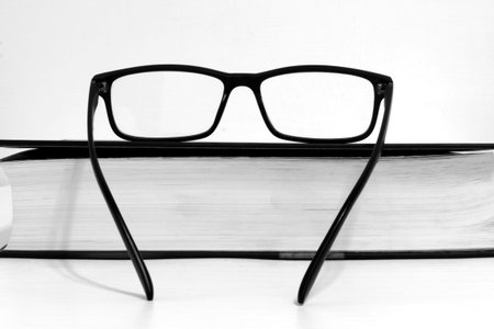 Glasses close up on closed book on blurred white background