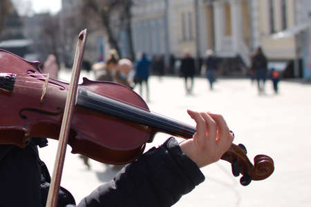 hands of street musician on violin on blurred background of pedestrian streetの写真素材