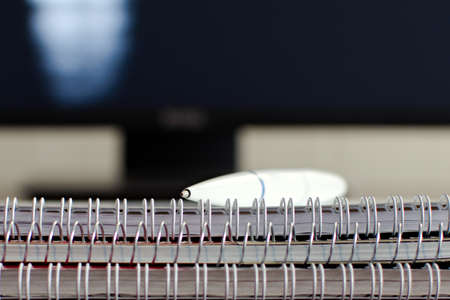 white ballpoint pen and notebooks with metal springs close up on blurred background of computer screenの写真素材