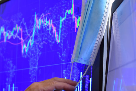 Disposable face mask with hand on blurred background of computer screen and monitor with stock chart