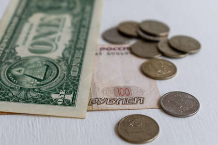 One dollar banknote and One hundred rubles banknote with rubles coins close-up on blurred background. Focus on foregroundの写真素材