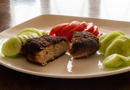Appetizing freshly cooked cutlet close-up with tomato and cucumber slices on white plate on the...