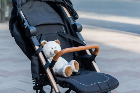 Soft toy teddy bear sitting in a baby stroller on blurred background of city streetの写真素材