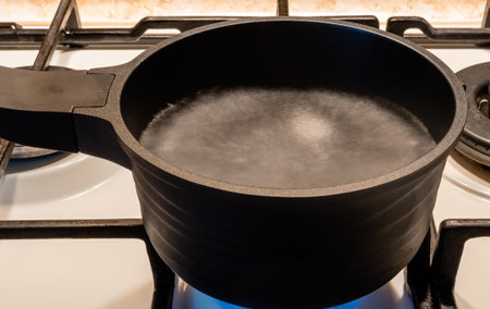Blurred motion image of boiling water in black metal pot on gas stove close-upの写真素材