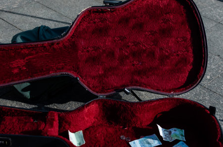 Open case for acoustic guitar on pavement of pedestrian street with banknotes