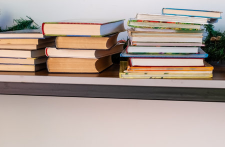 Stacks of books in colorful covers on table near white wallの写真素材