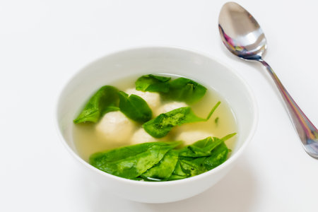 Appetizing light soup with chicken balls and herbs in white plate on white backgroundの写真素材