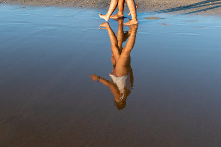 Blurred reflection of people walking along the beach in a thin film of water at low tideの写真素材