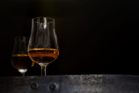 Whiskey glass close-up on black blurred background on oak barrel