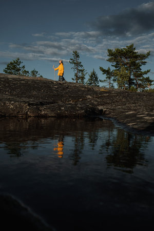 A girl in a yellow raincoat with a staff stands on the shore of Lake Ladoga