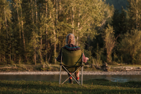 A girl sitting on a tourist chair on the bank of a mountain river.の写真素材