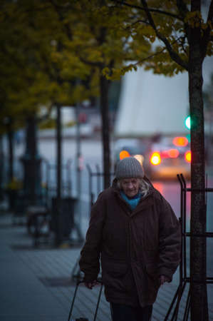 Photo pour VILNIUS, LITHUANIA - OCTOBER 6 2021: A grandmother with a trolley walks down the street in the evening - image libre de droit