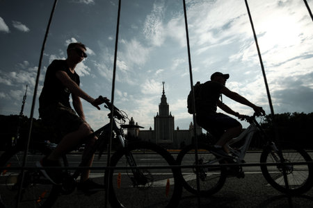 MOSCOW, RUSSIA - JULY 09 2022: Two cyclists ride past the MSU buildingのeditorial素材