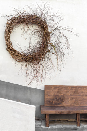 On the wall is a decorative wicker wicker wreath. A gray wall with a dark gray stripe in the background. Below is a wooden bench to sit on. Traditional seasonal decoration.の写真素材