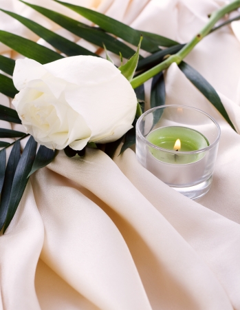 The white rose on a cream silk with a lighted candleの写真素材