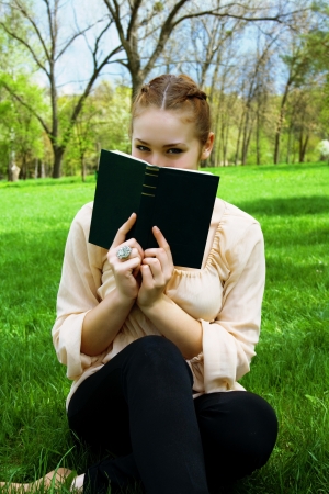 Woman hides her face behind a book sitting on green grassの写真素材