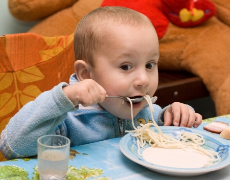 A baby eats spaghetti in her high chair の写真素材
