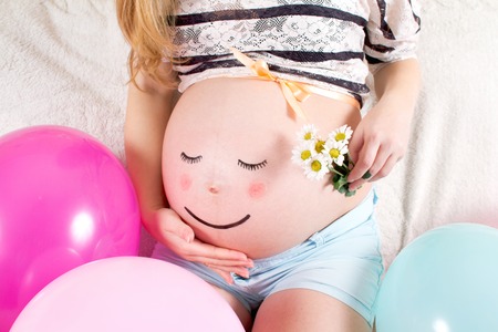 Pregnant woman with painted eyes on his stomach and mouthの写真素材