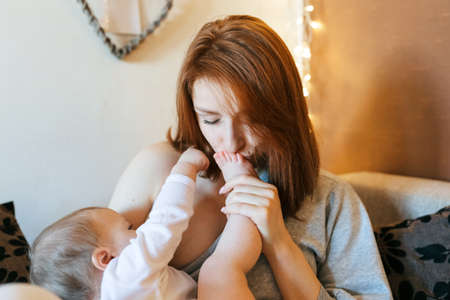 The little girl lies in her mother's arms and the mother kisses the baby's legの写真素材
