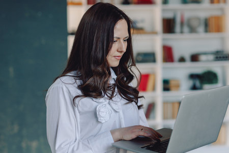 Beautiful woman working on laptop holding it in her hands. In the officeの写真素材