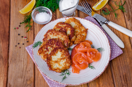 Potato pancakes with sour cream and salmon on a plate on a wooden backgroundの写真素材