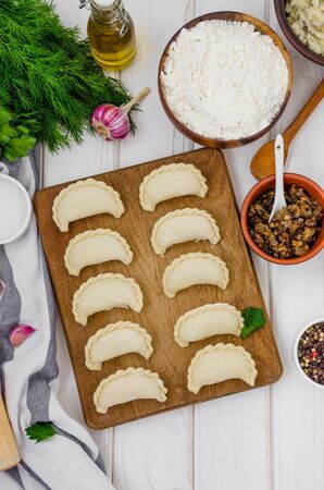 Uncooked vareniki (dumplings) on cutting wooden board on white background. Process of making vareniki with potatoes and fried mushrooms. Traditional Russian and Ukrainian dish.の写真素材
