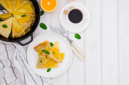 Crepe suzette with orange sauce and a cup of coffee on a white wooden background. Tasty and fragrant breakfast.の写真素材