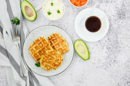 Cheese crispy waffles with cream cheese, smoked salmon and avocado for breakfast with a cup of coffee on a light stone background.の写真素材